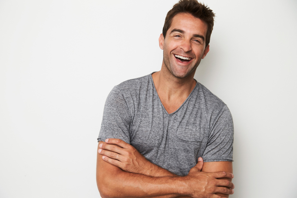 Man standing against a wall, smiling with his arms crossed.